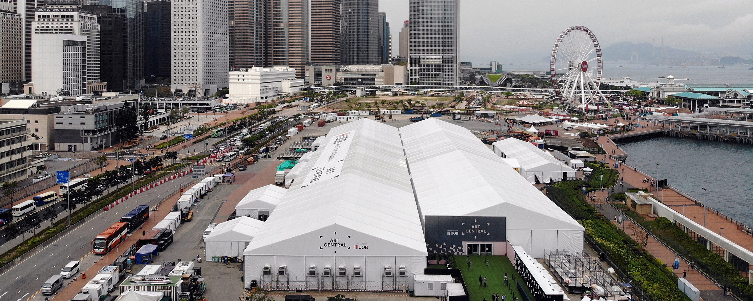Aerial view of a massive white exhibition tent complex set up in a city harbor area for international trade shows and commercial events.