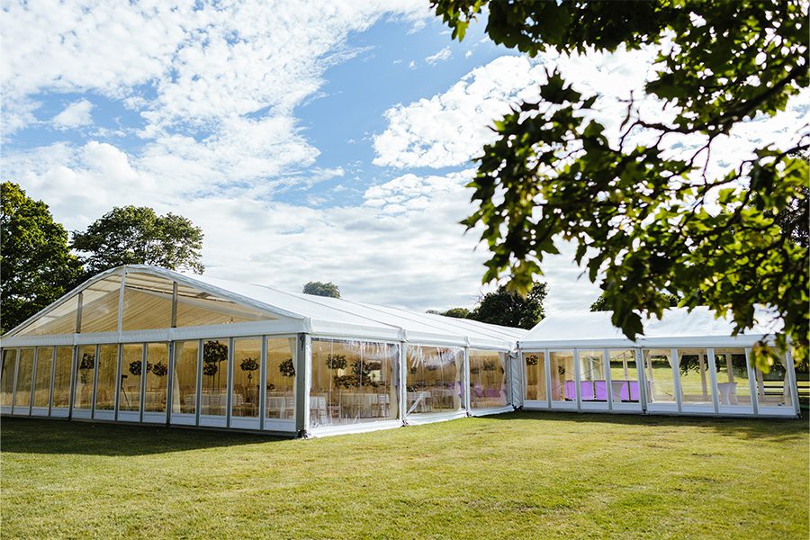 Elegant white outdoor wedding marquee featuring transparent window sidewalls and a classic A-frame structure for garden ceremonies.