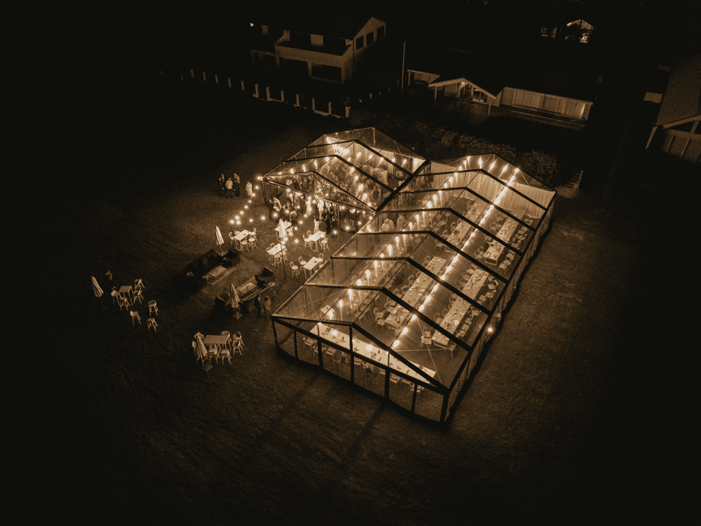 Aerial night view of a luxury transparent clear roof marquee with a black aluminum frame, illuminated for an evening outdoor party.
