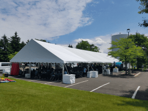 Open-sided outdoor dining canopy providing shade for a large company party on hard ground surface.