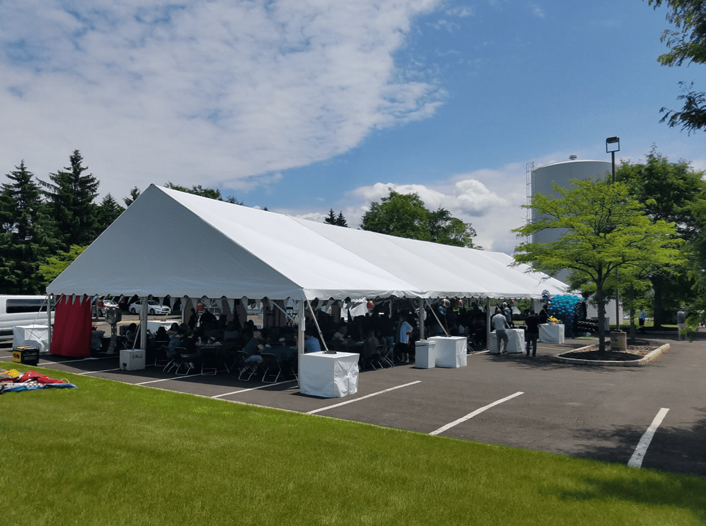 Open-sided outdoor dining canopy providing shade for a large company party on hard ground surface.