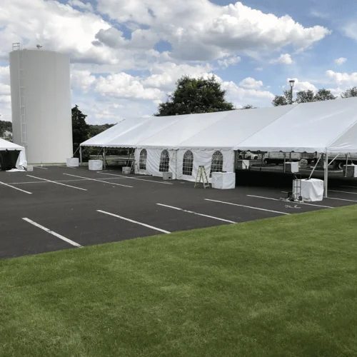 Long white aluminum frame tent setup on an asphalt parking lot featuring sidewalls with arched windows.