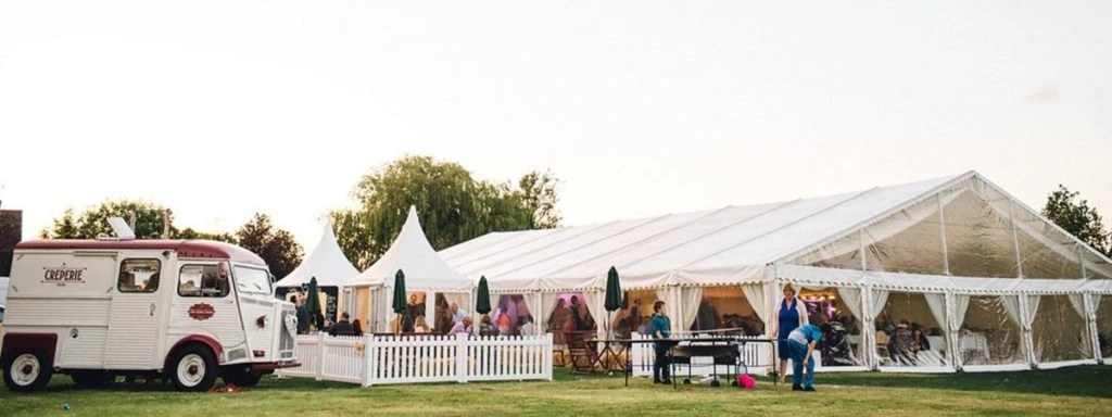Outdoor event setup featuring a vintage food truck serving guests beside a large white marquee tent with high peak pagoda entrances.