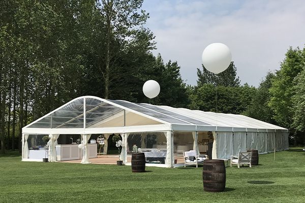 White Archy tent structure featuring a modern curved roof design and clear PVC sidewalls set up for an outdoor garden party.
