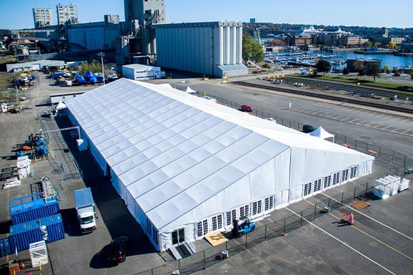 Large scale white A-frame clear span structure used as a temporary industrial warehouse or commercial facility at a port.
