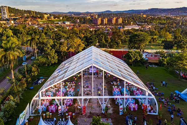 Aerial view of a large clear span curved tent with a fully transparent roof hosting an outdoor banquet event.